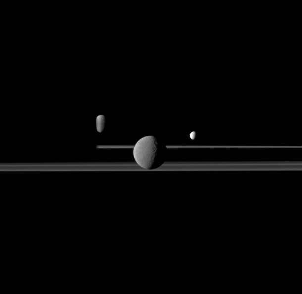 Rhea, Enceladus, and Dione join the rings of a darkened Saturn horizon