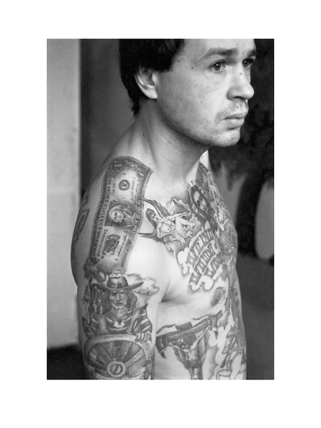 This convicts tattoos were applied in the camps of the Urals where the tattoo artists produce work of exceptional quality. Because they were so held in such high regard, criminals often attempted to be transferred there in order to be tattooed. The dollar bill on the shoulder signifies the bearers commitment to a life of crime.