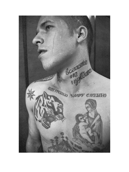 The tattoo on the neck reads 'I don't need happiness', beneath the neck 'I live in sin, I die laughing'. The scar on this criminals face is usually forcibly applied as a punishment to any convict who has informed or betrayed his fellow inmates.
