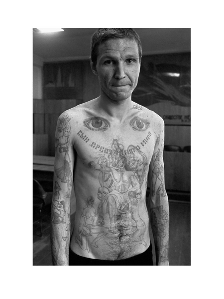 The eyes on the top of the chest signify 'I can see everything' and 'I am watching'. Text across the chest reads 'Son of the criminal world'. This photograph shows tattoos in a combination of old and new styles. In the new style a large number of almost random images on the convicts body. In the traditional style there is one large central tattoo on the chest, filling as much space as possible.