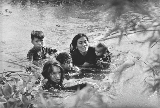 A mother and her children wade across a river to escape US bombing. The US Air Force had evacuated their village because it was suspected of being used as a base camp by the Vietcong
