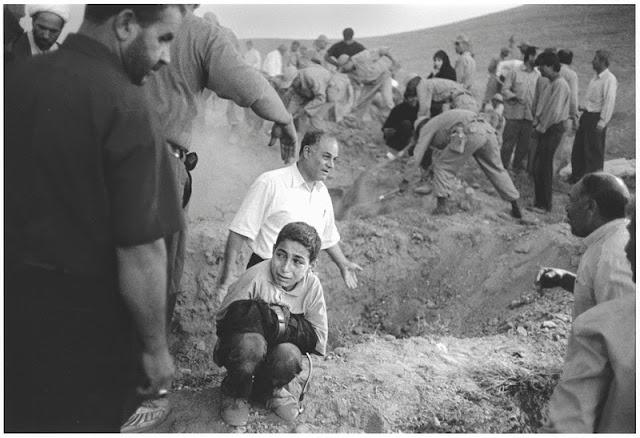 A boy holds his dead father's trousers as he squats beside the spot where his father is to be buried, surrounded by soldiers and villagers digging graves for victims of an earthquake in Armenia