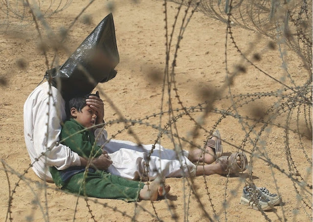 An Iraqi man comforts his four-year-old son at a holding center for prisoners of war, in the base camp of the US Army 101st Airborne Division near An Najaf. The boy had become terrified when, according to orders, his father was hooded and handcuffed. A soldier later severed the plastic handcuffs so that the man could comfort his child. Hoods were placed over detainees' heads because they were quicker to apply than blindfolds. The military said the bags were used to disorient prisoners and protect their identities. It is not known what happened to the man or the boy