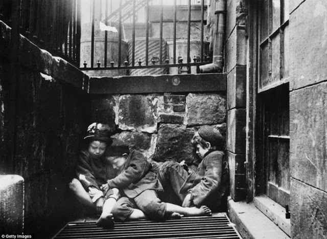 Three young street children huddle together over a grate for warmth in an alleyway off Mulberry Street, Manhattan