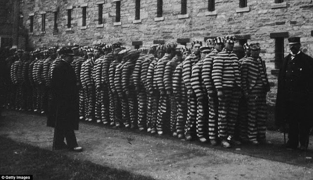 A group of prisoners in striped suits and hats at The Lock-step Penitentiary on Blackwell's Island around 1890