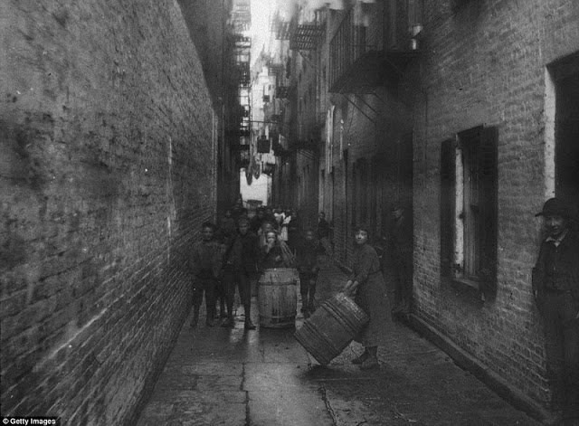 Children play with barrels under the washing hung between tenements in Gotham Court, Cherry Street around 1890