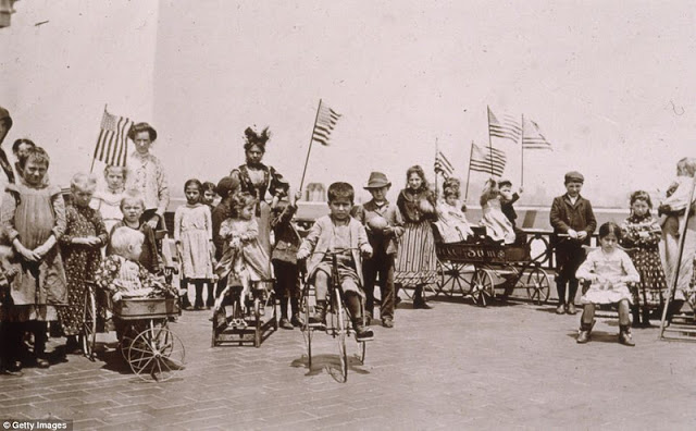 Children holding American flags while riding tricycles and wagons on the rooftop garden of Ellis Island were the offspring of detained or waiting immigrants