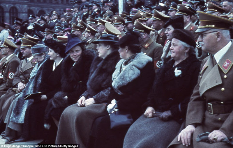 Female guests sit in their fur coats among Nazi officers at a military parade for Hitler's 50th birthday in Berlin