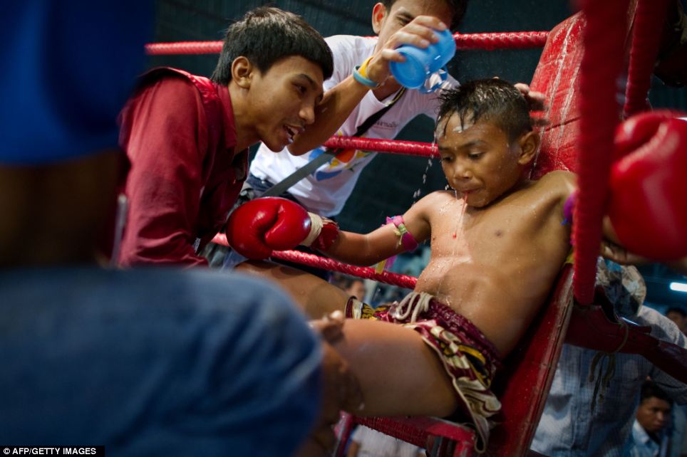 A boxer spits blood whilst listening to advice from his coach between rounds in his corner as the crowds cheer on the children fighting