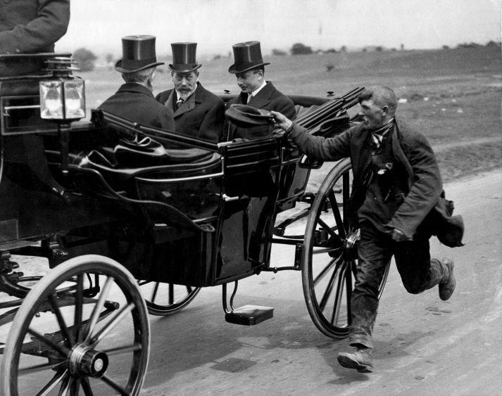 A beggar running alongside King George Vs coach. England, c. 1920