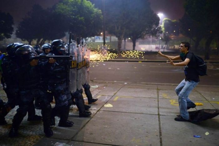 A Brazilian protester stands before gunfire during protests against corruption and police brutality.
