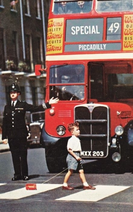 A boy crosses a London street in the 1960s with a toy double decker.