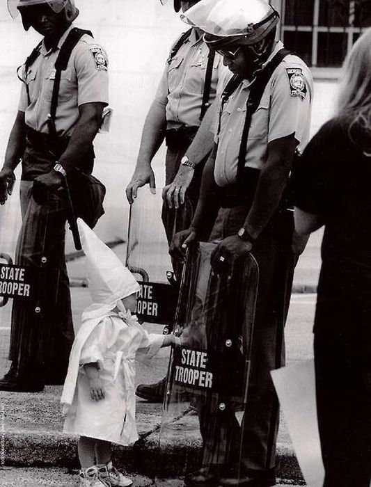 The child of a KKK member touches his reflection in an African American police officer's riot shield during a demonstration. 1992