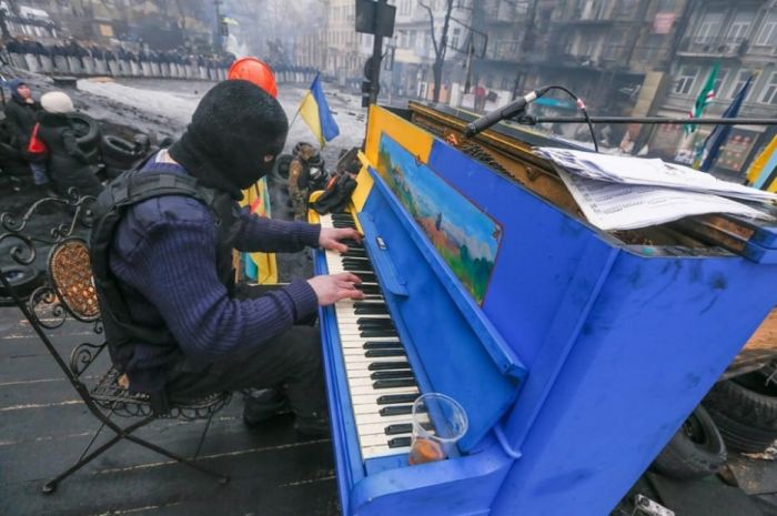Protester plays piano over the sounds of chaos, with riot police in the backdrop
