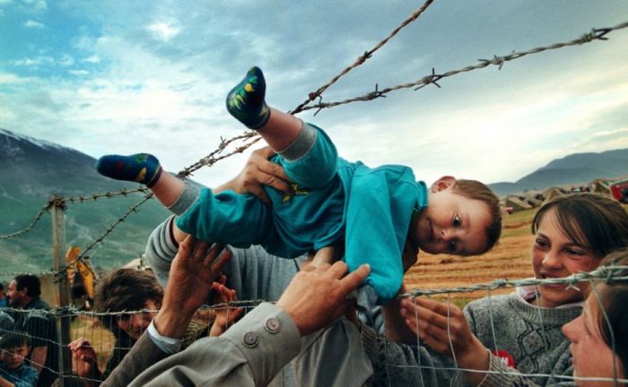 Agim Shala is passed through a barbed wire fence to his grandparents at a camp for refugees of the Kosovo War