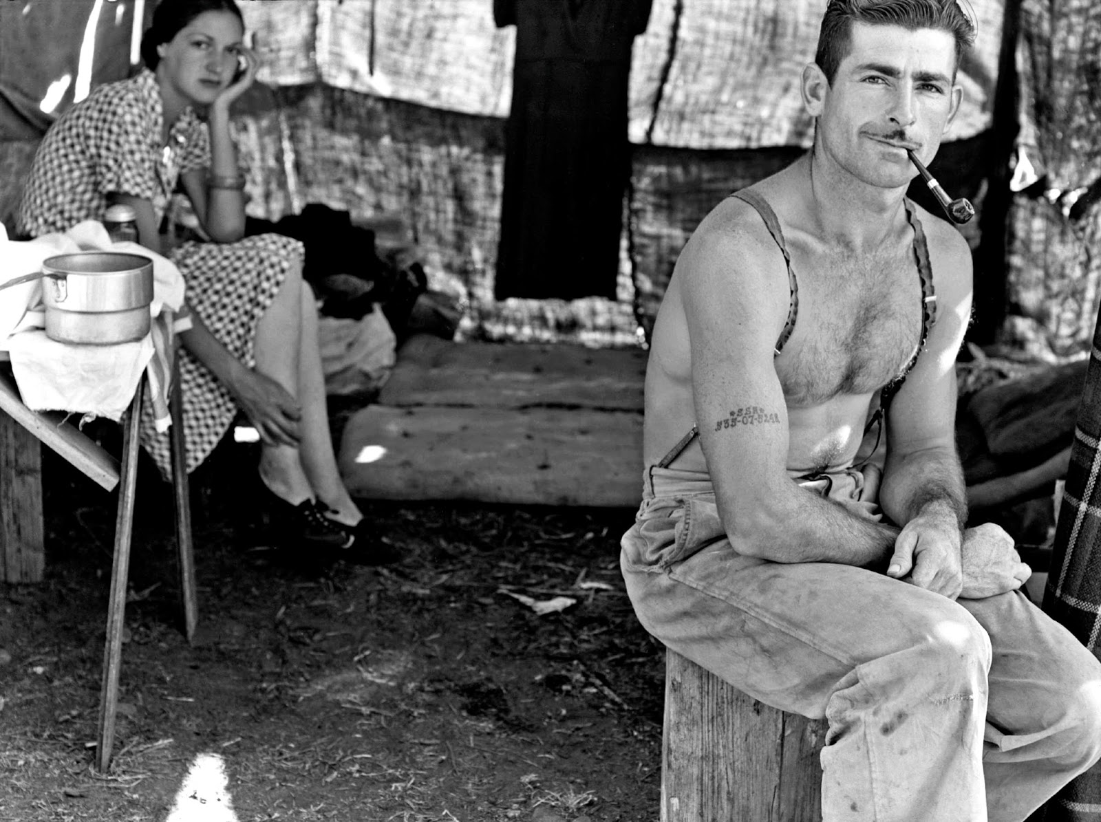 Unemployed lumber worker goes with his wife to the bean harvest. Note social security number tattooed on his arm, Oregon, 1939 by Dorothea Lange.