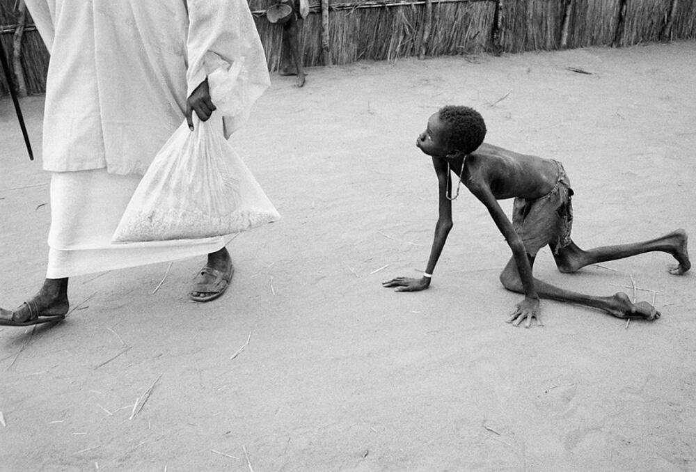 A well-nourished Sudanese man steals maize from a starving child during food distribution at a humanitarian aid feeding center in Ajiep, Sudan in 1998