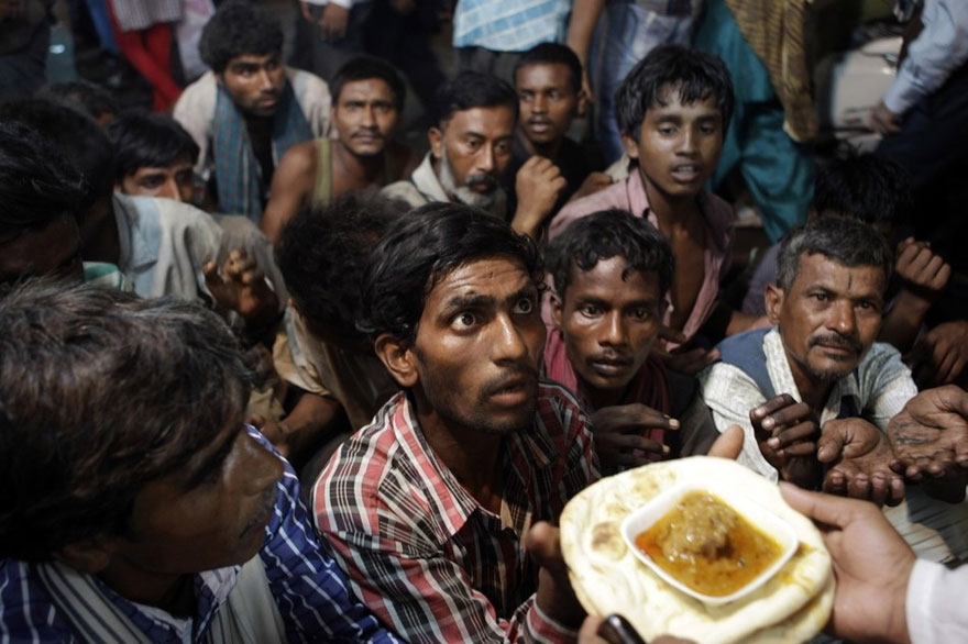 Indian homeless men wait to receive free food outside a mosque in New Delhi, India