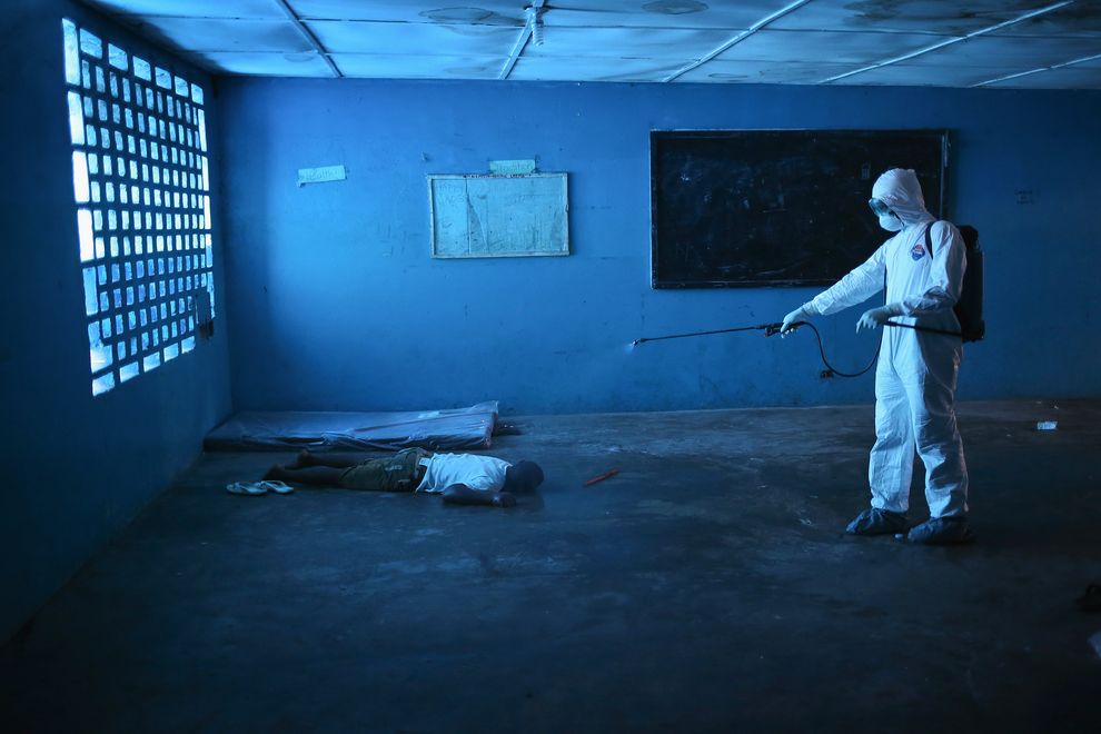 A health worker disinfects a corpse in an Ebola isolation ward, once a primary school, in Monrovia, Liberia