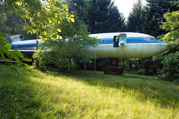 The airplane sits on a forested private property, with wilderness all around
