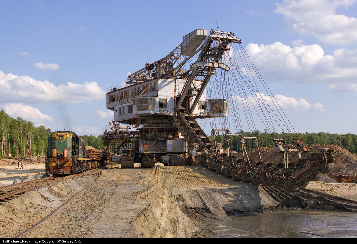 Massive Russian dragline ? crane scooping sand and the loading the train next to it.
