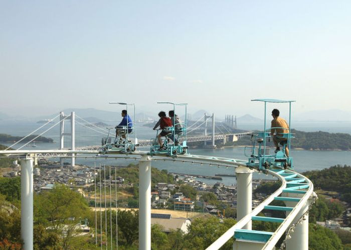 Tourists ride a pedal-powered sky cycle roller coaster at Washuzan Highland Amusement Park in Kurashiki, Japan. Washuzan Highland Amusement park overlooks a panoramic view of islands on the Seto Inland Sea.