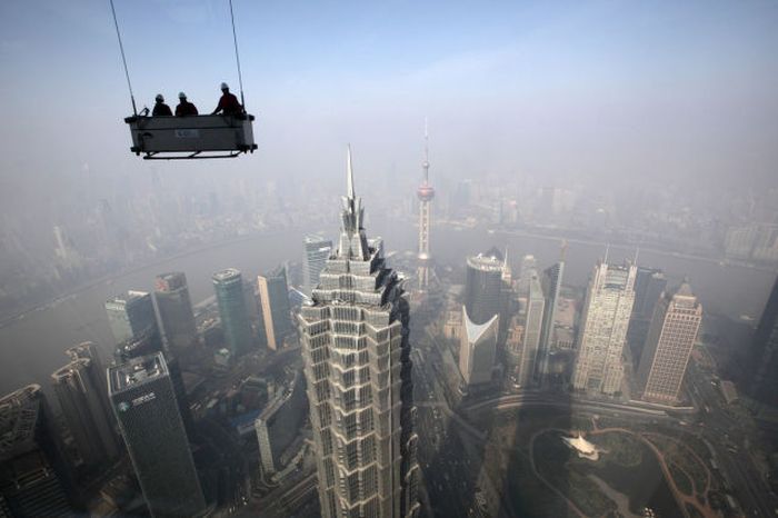 Workers stand in a suspended platform ready to clean windows at the Shanghai World Financial Center in the Pudong area of Shanghai, China. China's economic growth accelerated for the first time in two years as government efforts to revive demand drove a rebound in industrial output, retail sales and the housing market.