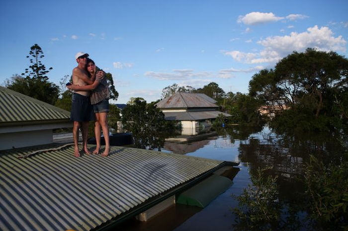 A man comforts his daughter on their roof as they inspect damage to their neighbourhood as parts of southern Queensland experiences record flooding in the wake of Tropical Cyclone Oswald in Bundaberg, Australia.