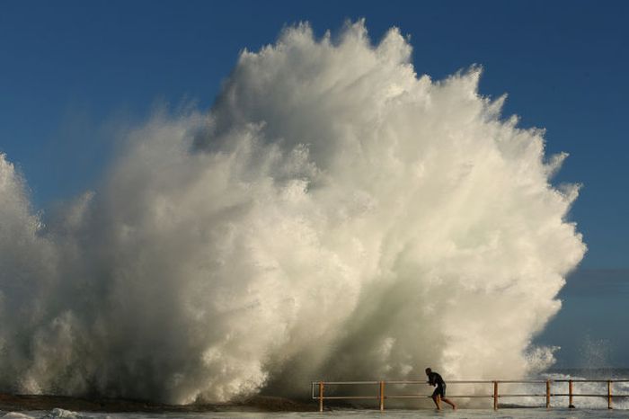 A man hangs onto the railing of North Curl Curl ocean pool after winds and rain battered Sydney last night producing large swell in Sydney, Australia. Parts of Sydney are experienced record rainfall after ex-cyclone Oswald swept through the city last night.