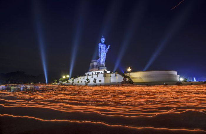 People walk around the Buddha Statue holding candles for prayers during Makha Bucha Day at Buddhist Park in Nakhon Pathom, Thailand.