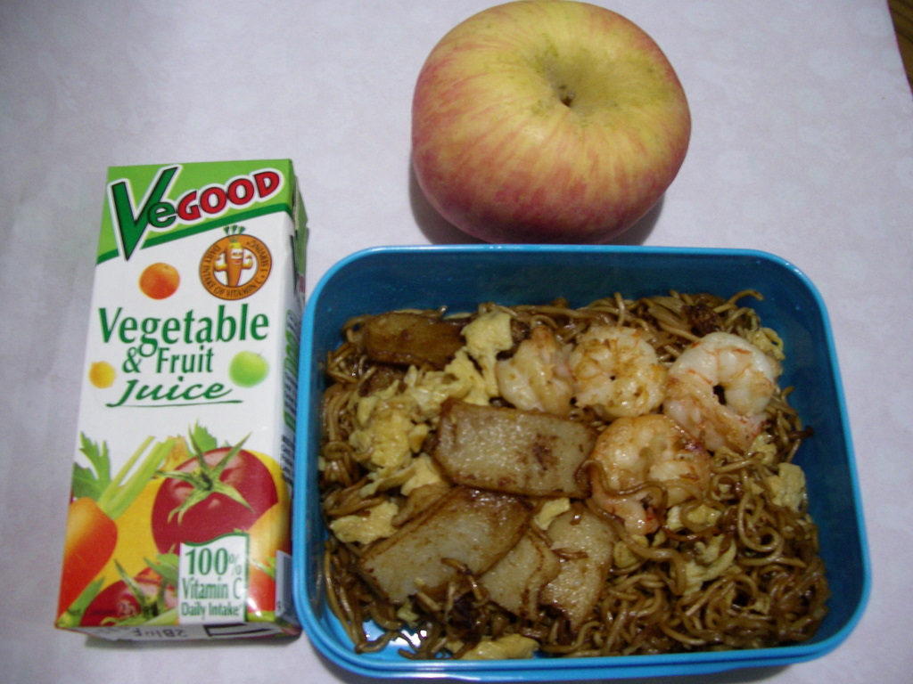 Country: Malaysia. Contents: Noodle, prawn, fish-cake, eggs, a packet of vegatable and fruit juice, and an apple.