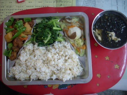 Country: Taiwan. Contents: On the left: sweet and sour pork with pineapple, radish, carrots and green pepper, middle: vegetable stir fry with garlic, on the right: fish ball stew with cabbage, carrots and wood ear mushroom, and soup: seaweed and egg drop.