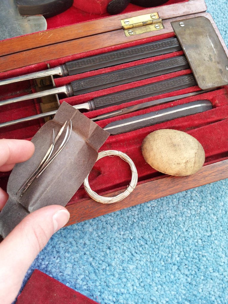 Sewing needles and metal wire for thread, along with a small object used to hammer the needles through.
