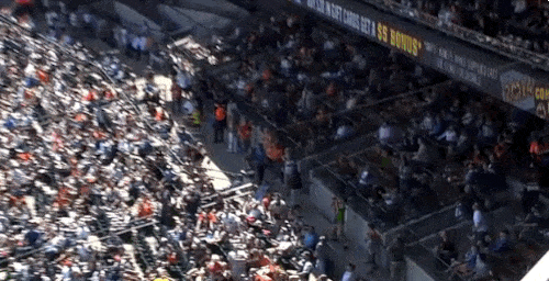 Many holds toddler in one hand and catches a fly ball with the other at a baseball game.