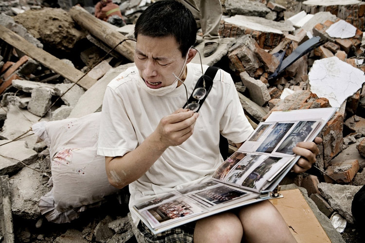 man cries as he flips through a family album he found in the rubble of his old house following an earthquake in Sichuan.