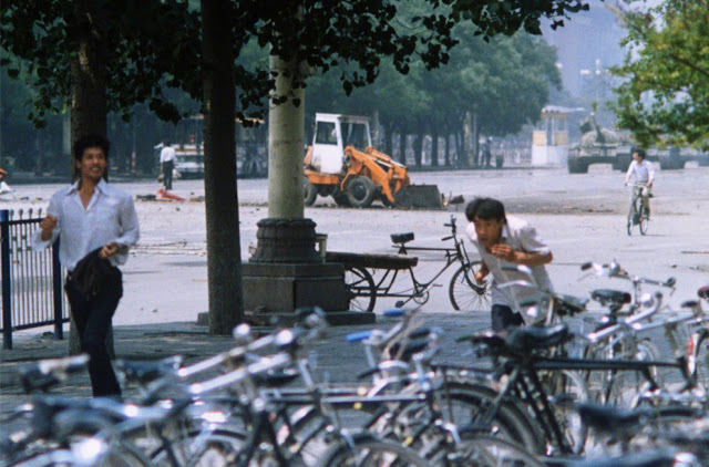 A new angle of his act of protest, now at a distance. Tank Man can be seen through the trees on the left, and the tanks can be seen on the far right.