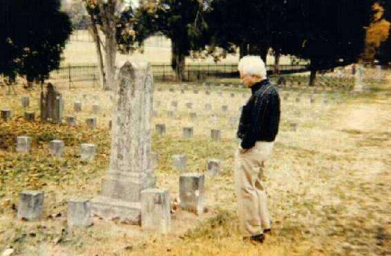 This photo was taken at a cemetery in Tennessee. As the man in the photo looks down at a tombstone, an image of a Confederate soldier can be seen in the upper right corner of the picture.