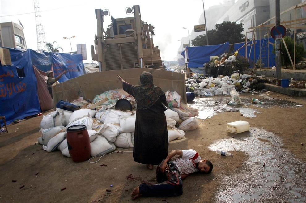 A woman tries to stop a military bulldozer from hurting a wounded person after clashes between security forces and opposition groups that left hundreds dead in Cairo