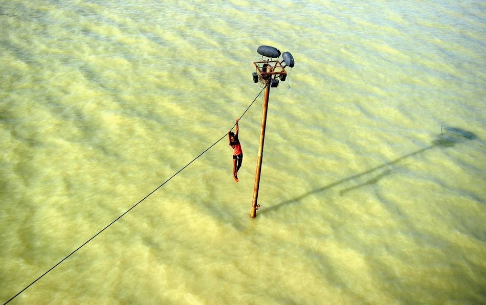 An Indian youth dangles from a power line before diving into the floodwaters of an overflowing Ganges river in Allahabad in August.