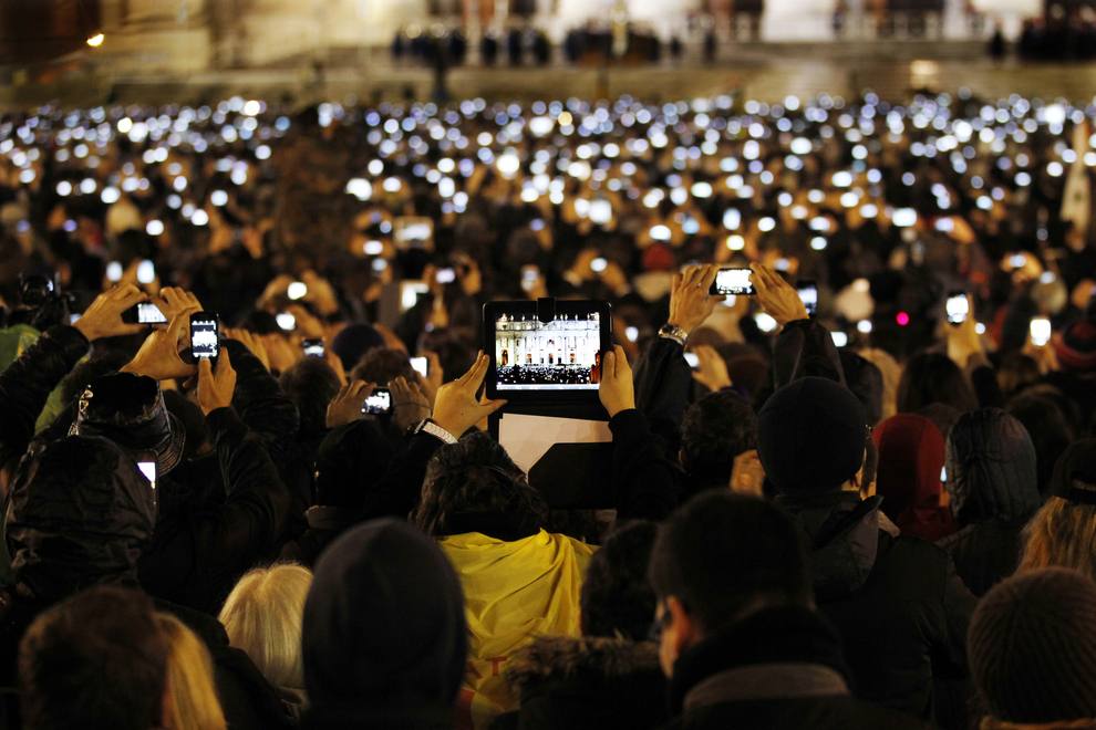 Catholics take photos with their phones and tablets of the newly-elected Pope Francis as he speaks from the central balcony of St. Peter’s Basilica at the Vatican.