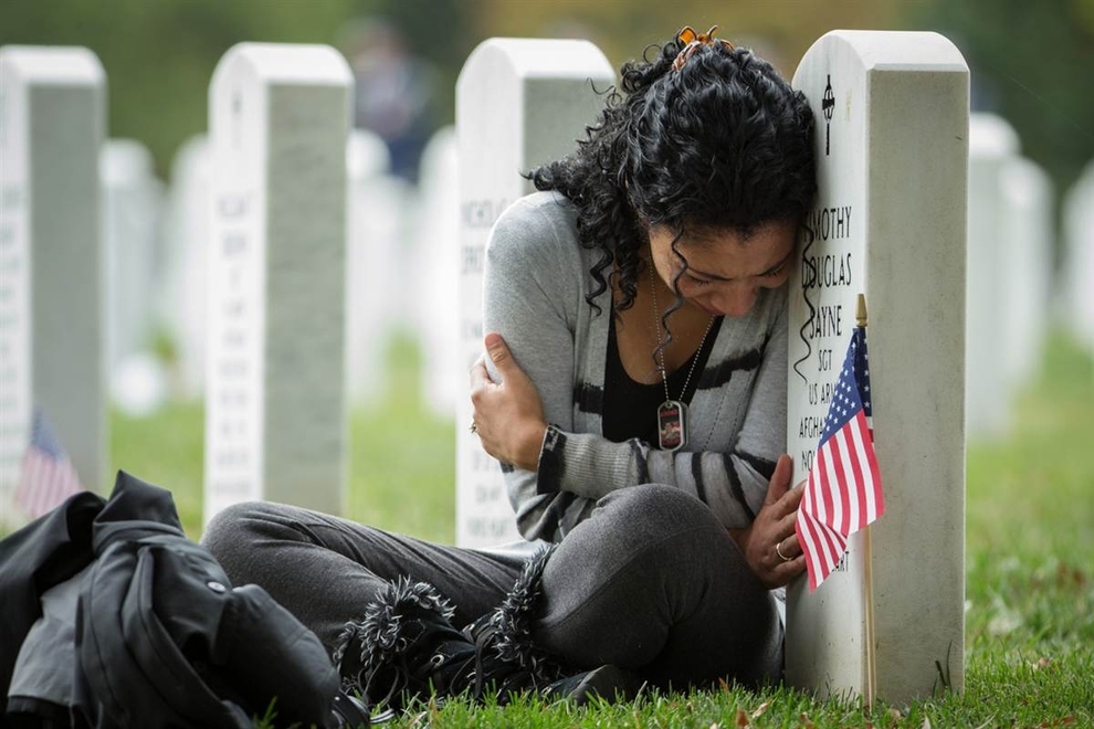 Thania Sayne leans on the headstone marking the grave of her husband, who was killed in Afghanistan in 2011, at Arlington National Cemetery