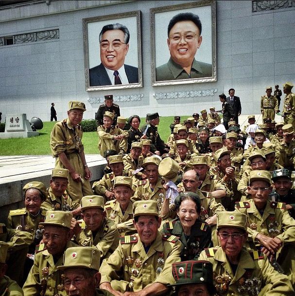 North Korean veterans of the Korean War sitting under the two Kim’s portraits