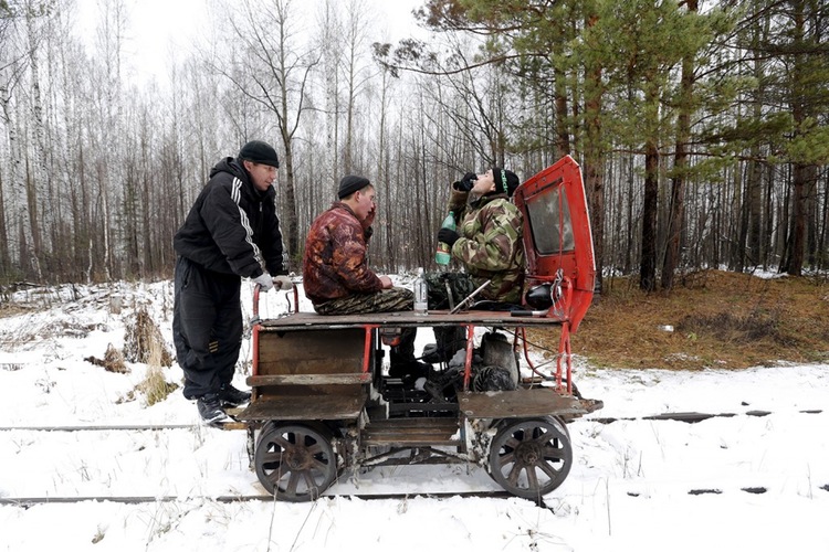 Three Russian men drink vodka as they travel along the Alapayevsk railway on a cart, one of the most popular forms of transport in this remote region of the Urals