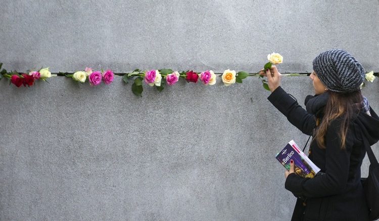 A woman places a rose in the cracks of the Berlin Wall as Germans celebrate the 26th anniversary of its fall.