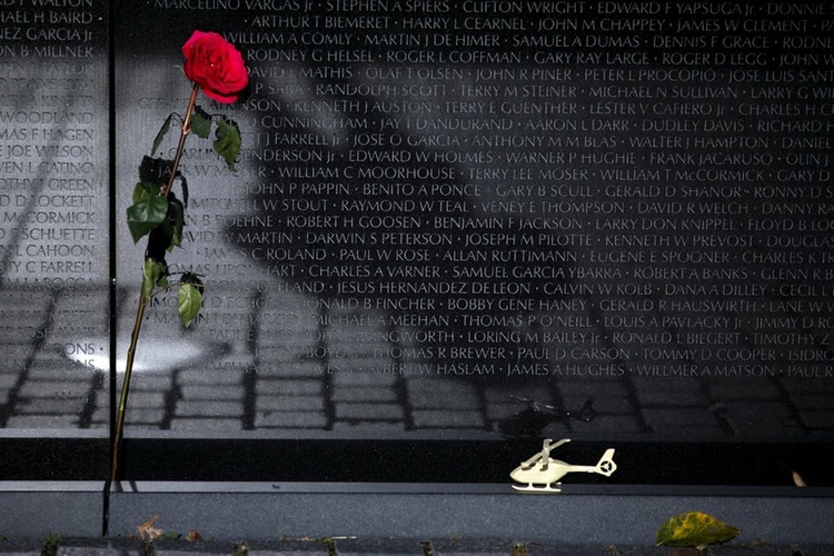 A rose and a toy helicopter are laid next to the Vietnam Veterans Memorial wall during Veterans Day.