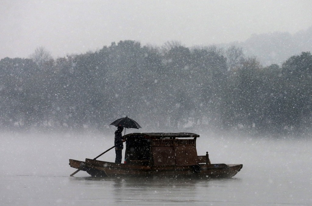 A man holds an umbrella to shield against snowfall as he rows a boat on the West Lake in Hangzhou, China.