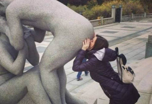 Woman kissing the anus of a statue in an outdoor setting