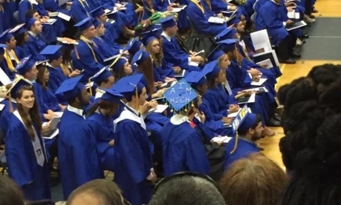 Picture of a graduating class and one of the caps has AIM HIGH written atop it.