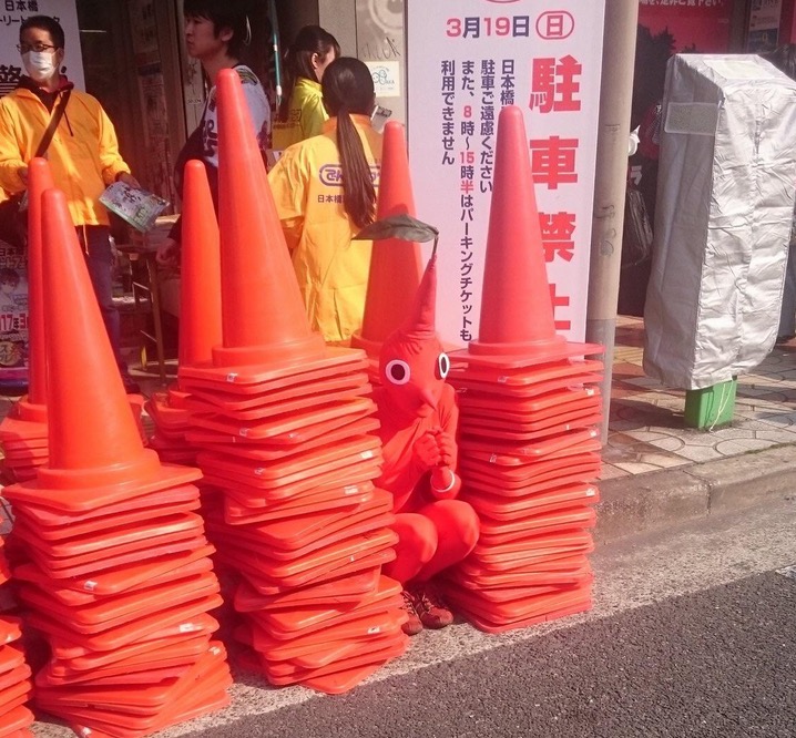 Person dressed as traffic cone hiding among traffic cones.