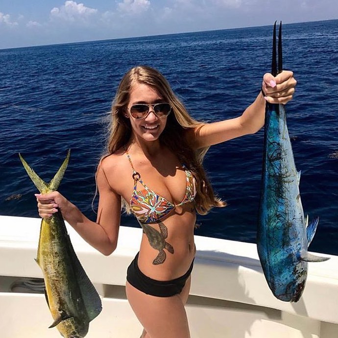 Busty girl in a bikini holding up two very large fish.
